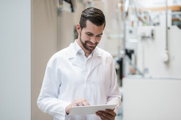 Man wearing lab coat in factory using tablet - DIGF03391