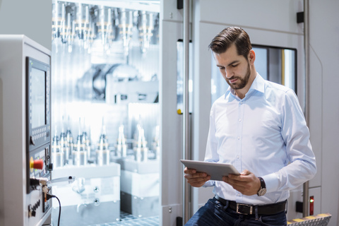 Businessman at machine in factory looking at tablet stock photo