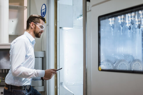 Geschäftsmann mit Tablet, der eine Schutzbrille trägt und eine Maschine in einer Fabrik prüft - DIGF03396