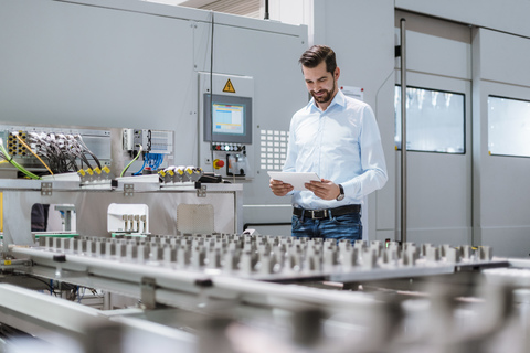 Businessman at machine in factory looking at tablet stock photo