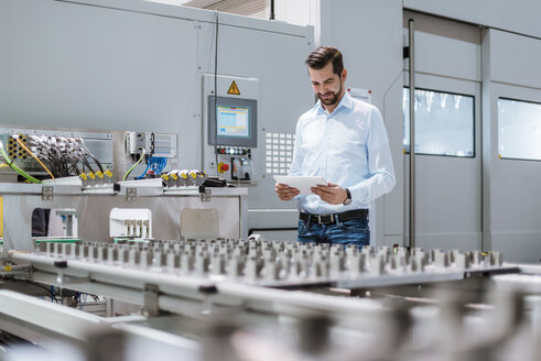 Geschäftsmann an einer Maschine in einer Fabrik mit Blick auf ein Tablet - DIGF03399