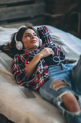 Trendige junge Frau hört Musik, während sie zu Hause auf dem Bett liegt - FSIF01839