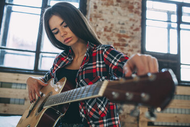 Niedriger Blickwinkel auf eine junge Frau, die zu Hause Gitarre spielt - FSIF01841