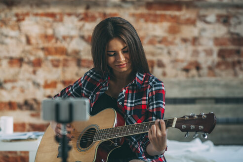 Smartphone im Einbeinstativ mit einer Frau, die zu Hause Gitarre spielt - FSIF01846