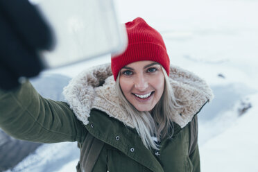 Lächelnde junge Frau, die im Winter ein Selfie mit ihrem Smartphone macht - FSIF01852