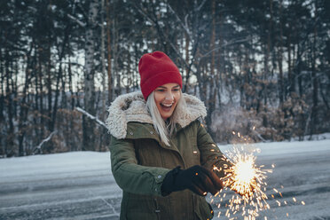 Happy woman holding sparklers while standing on field during winter - FSIF01854
