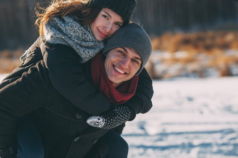 Porträt eines glücklichen Mannes, der eine Frau im Winter huckepack nimmt, lizenzfreies Stockfoto