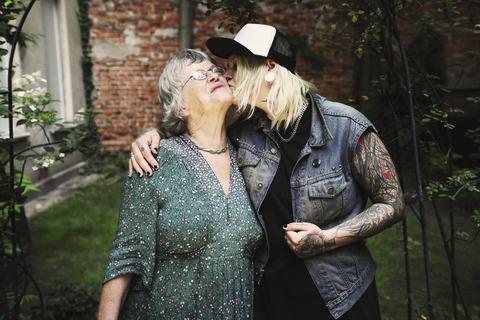 Daughter kissing mother while standing in back yard stock photo