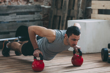 Engagierter Mann beim Training mit Kettlebells im Fitnessstudio - FSIF01892