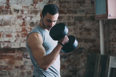 Entschlossener junger Mann hebt eine Hantel im Fitnessstudio - FSIF01893