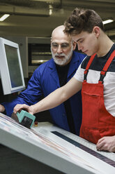 Arbeiter prüfen die Druckqualität mit einem Scanner an der Druckmaschine - FSIF01911