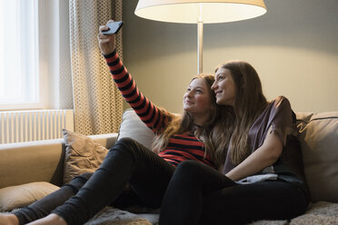 Siblings taking selfie through mobile phone in living room - FSIF01926
