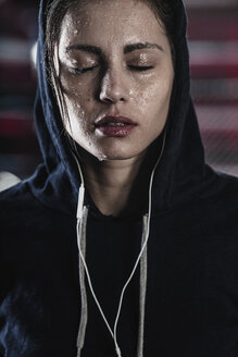Frau im Kapuzenshirt mit Schweiß im Gesicht im Fitnessstudio - FSIF01943