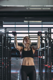 Vorderansicht einer Sportlerin bei Klimmzügen im Fitnessstudio - FSIF01949