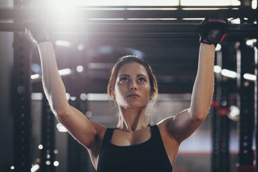 Nahaufnahme einer jungen Frau bei Klimmzügen im Fitnessstudio - FSIF01950