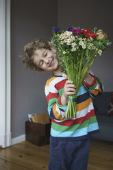 Glücklicher Junge hält Blumenstrauß zu Hause stehend - FSIF01955