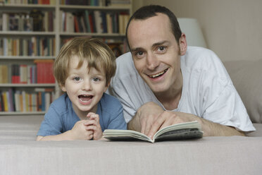 Portrait of smiling father and son lying on bed with book at home - FSIF01957