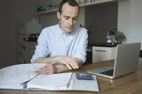 Seriöser Mann bei der Arbeit mit Laptop und Datei zu Hause - FSIF01959