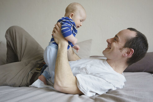 Lächelnder Vater hält seinen Sohn und liegt zu Hause auf dem Bett - FSIF01963