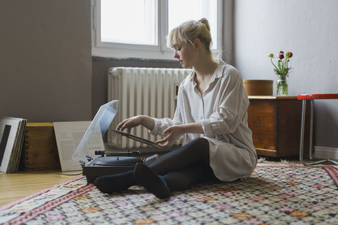 Frau in voller Länge beim Abspielen einer Schallplatte, während sie zu Hause sitzt - FSIF01974