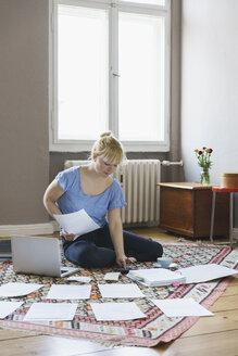 Frau erledigt Papierkram, während sie zu Hause auf dem Teppich sitzt - FSIF01975