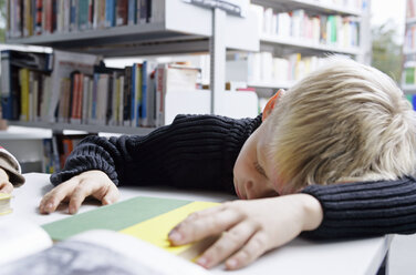 Ein Junge hält ein Nickerchen auf einem Schreibtisch in einer Bibliothek - FSIF02054