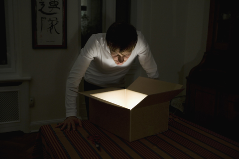 Young man staring into illuminated cardboard box stock photo