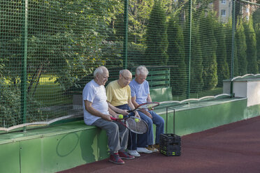 Ältere Freunde mit Tennisschlägern sitzen am Zaun des Tennisplatzes - FSIF02163