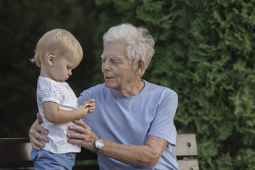 Smiling grandfather playing with girl on park bench - FSIF02166