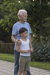 Lächelnder Großvater steht mit seinem Enkel auf dem Fußweg im Park - FSIF02167