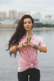 Junge Frau mit geschlossenen Augen übt Yoga in Gebetshaltung am Fluss - FSIF02183