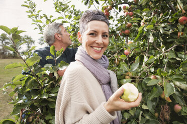 Portrait of happy woman eating apple in orchard - FSIF02191