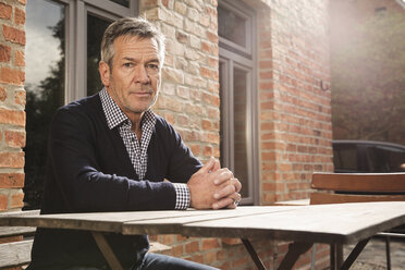 Portrait of mature man sitting at table outside house - FSIF02193