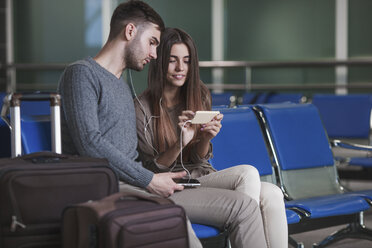 Young couple listening music through smart phone while waiting in airport - FSIF02215