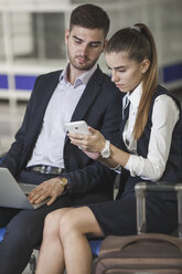 Junges Geschäftspaar benutzt Smartphone beim Warten am Flughafen - FSIF02218