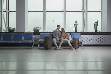 Junges Paar mit Gepäck auf Stühlen am Flughafen sitzend - FSIF02219