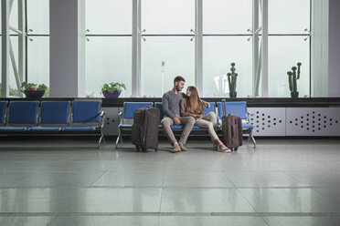 Young couple with luggage sitting on chairs at airport - FSIF02219