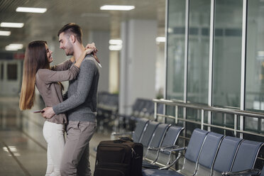 Seitenansicht eines glücklichen jungen Paares, das sich am Flughafen umarmt - FSIF02221