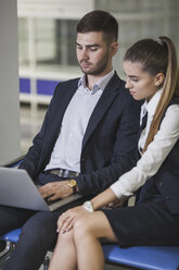 Young businesswoman sitting by businessman using laptop at airport - FSIF02225