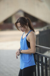 Frau schaut auf Fitness-Tracker, während sie an einem Geländer im Park steht - FSIF02230