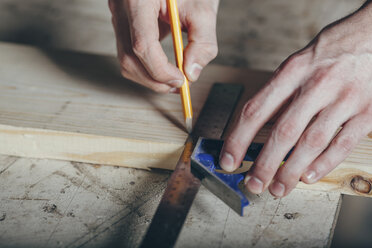 Abgeschnittene Hände eines Zimmermanns, der in der Werkstatt mit Bleistift und Lineal ein Brett anzeichnet - FSIF02244