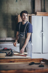 Carpenter holding pencil while looking away at workshop - FSIF02251