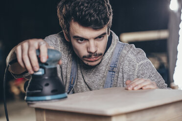 Schreiner bei der Arbeit mit einer elektrischen Schleifmaschine an einem Holzbrett in der Werkstatt - FSIF02258