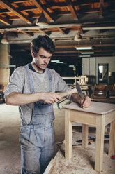 Carpenter hammering nail into wooden stool at workshop - FSIF02259