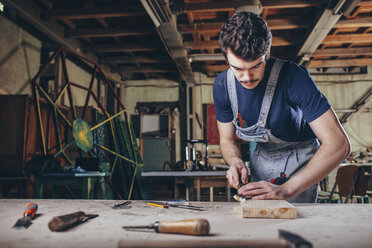 Schreiner mit Meißel auf einem Holzbrett in der Werkstatt - FSIF02260