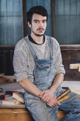 Porträt eines jungen Arbeiters, der mit Handwerkzeugen auf einer Bank sitzt - FSIF02261