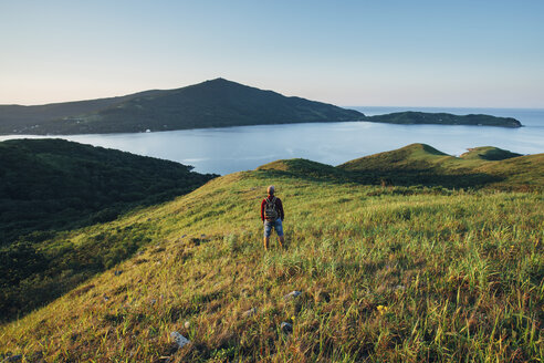 Rear view of hiker standing on grassy field while looking at East sea against sky - FSIF02263