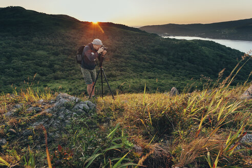 Mann beim Fotografieren auf einer Wiese bei Sonnenuntergang - FSIF02264