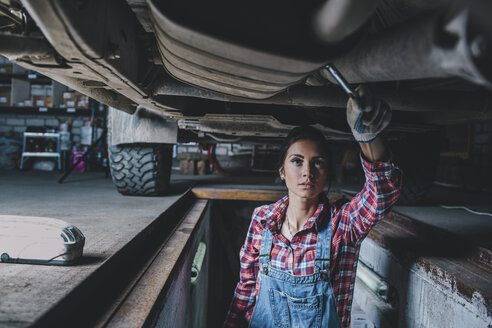 Female mechanic working underneath car at garage - FSIF02274