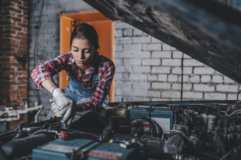 Mechanikerin repariert Automotor in einer Werkstatt, lizenzfreies Stockfoto